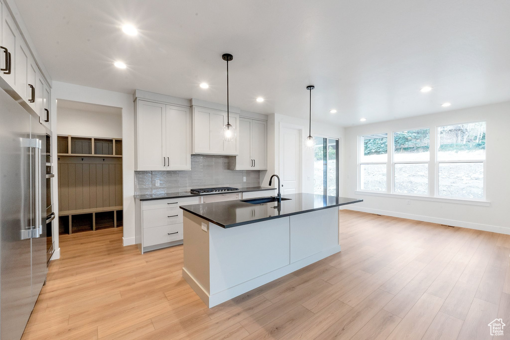 Kitchen featuring sink, an island with sink, hanging light fixtures, white cabinets, and light hardwood / wood-style flooring