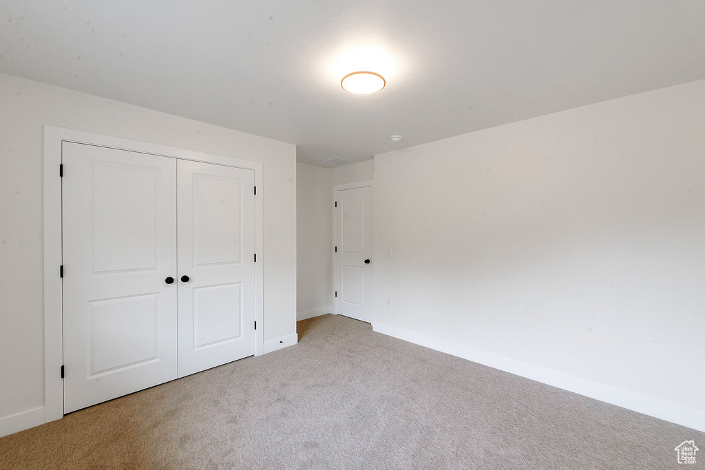 Unfurnished bedroom with light colored carpet and a closet