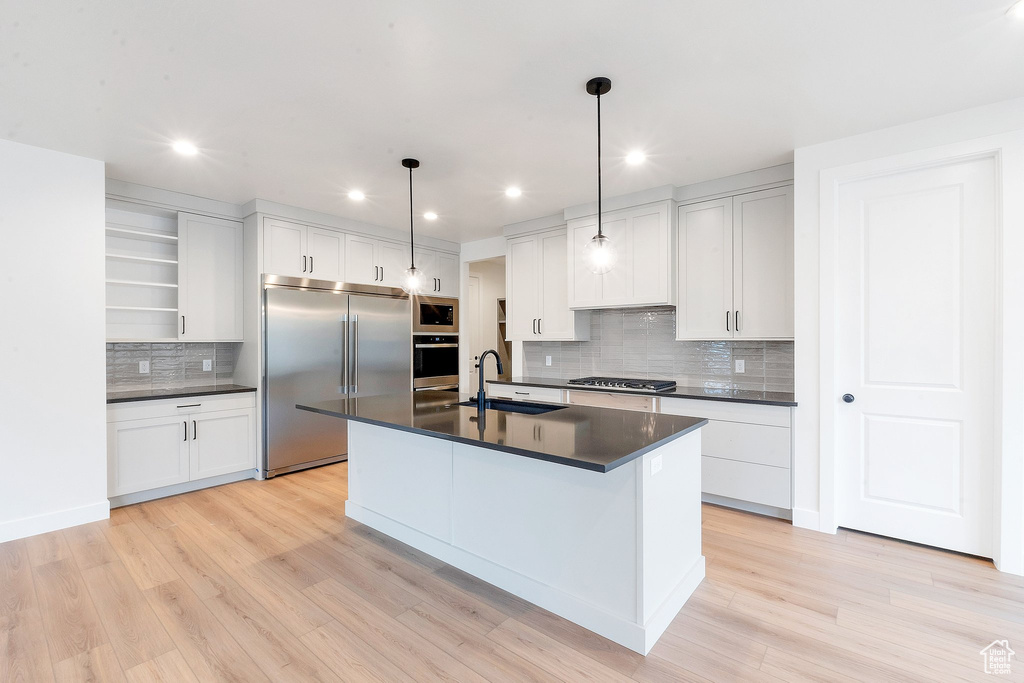 Kitchen featuring sink, built in appliances, decorative light fixtures, and white cabinetry