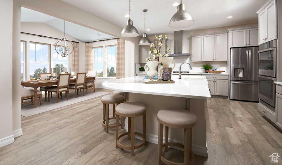 Kitchen with lofted ceiling, light hardwood / wood-style flooring, appliances with stainless steel finishes, decorative light fixtures, and a center island with sink