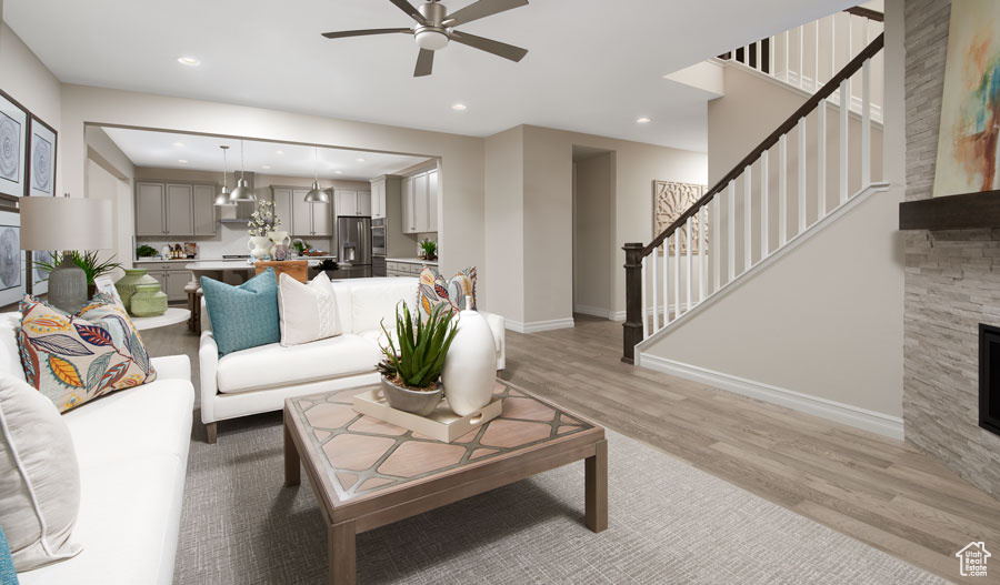 Living room with a stone fireplace, light hardwood / wood-style flooring, and ceiling fan