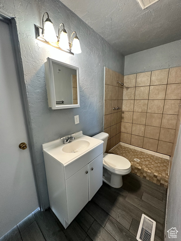 Bathroom featuring vanity, tiled shower, toilet, and a textured ceiling