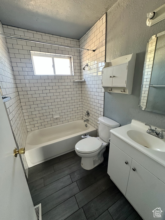 Full bathroom featuring tiled shower / bath, vanity, toilet, and a textured ceiling