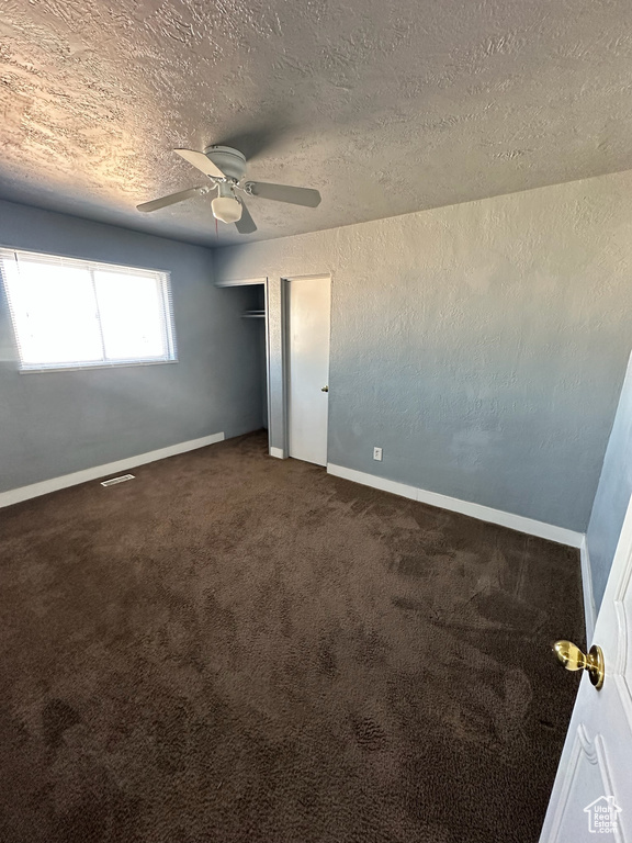 Unfurnished bedroom featuring ceiling fan, a textured ceiling, and dark colored carpet