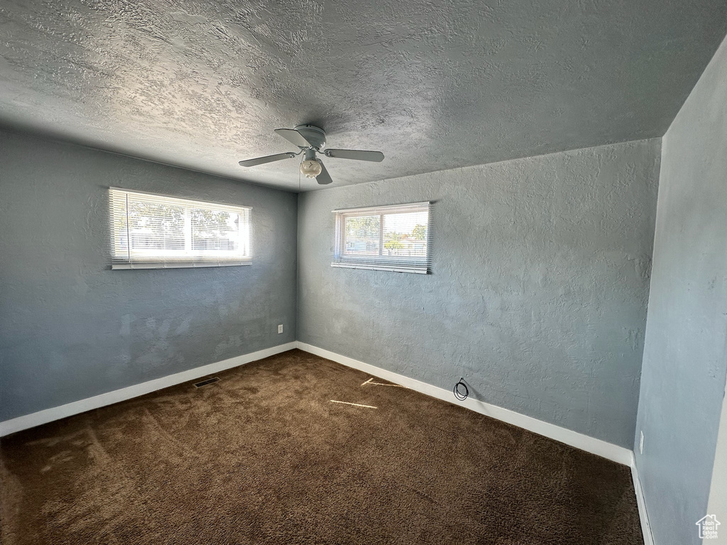 Empty room with ceiling fan, a textured ceiling, and dark colored carpet