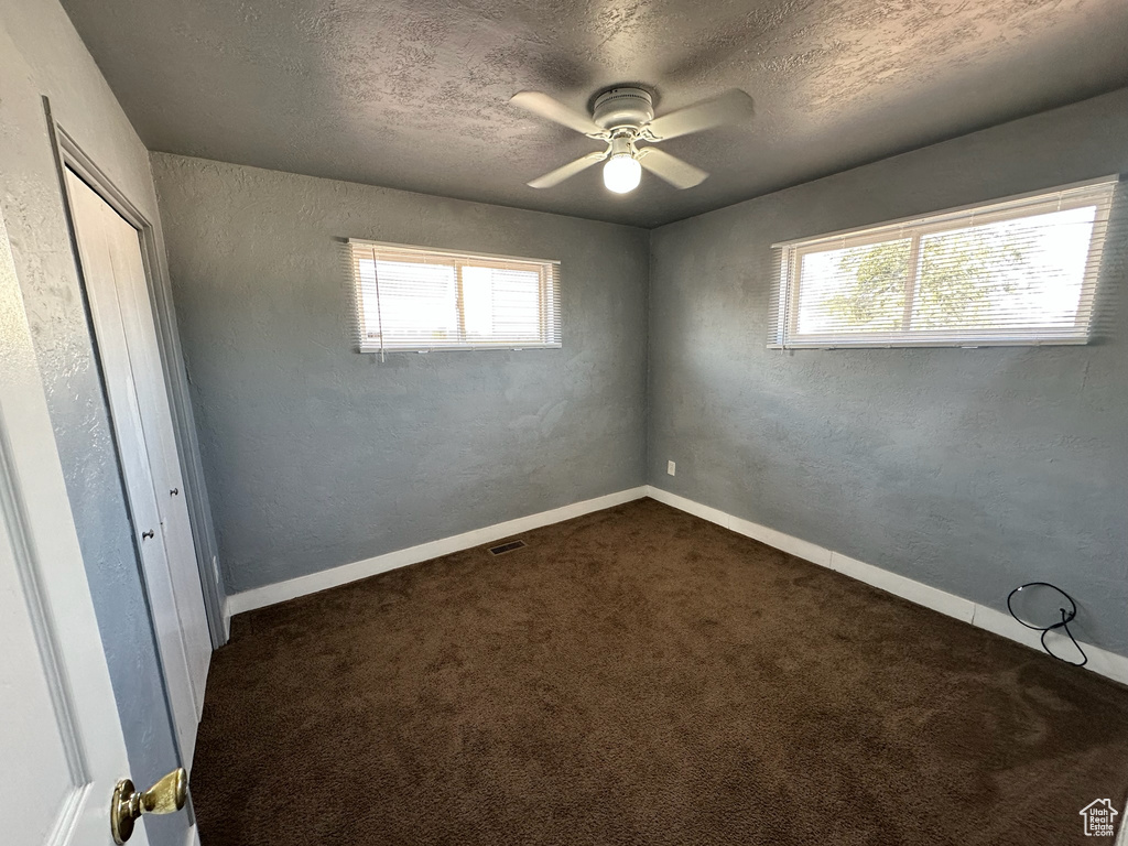 Unfurnished bedroom with dark colored carpet, multiple windows, ceiling fan, and a textured ceiling