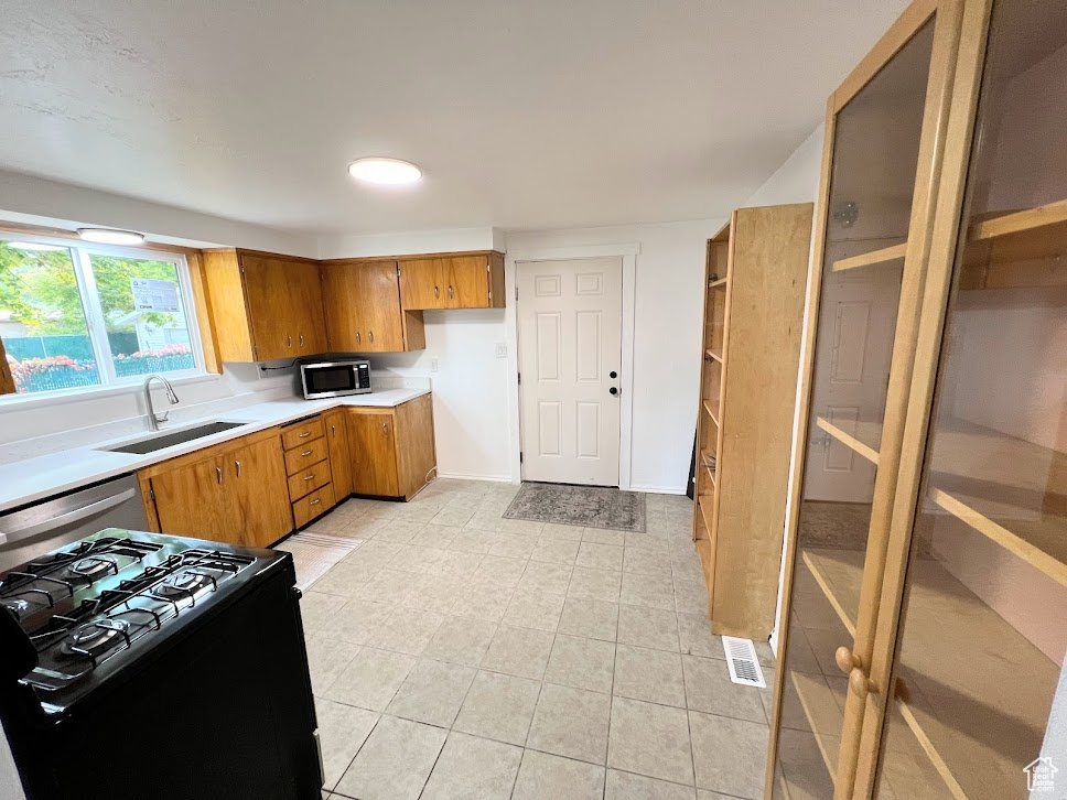 Kitchen with black gas stove, sink, and light tile patterned floors