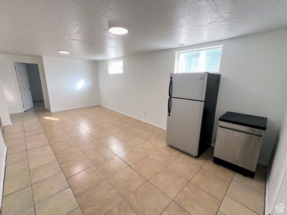 Basement featuring fridge, light tile patterned floors, and a textured ceiling