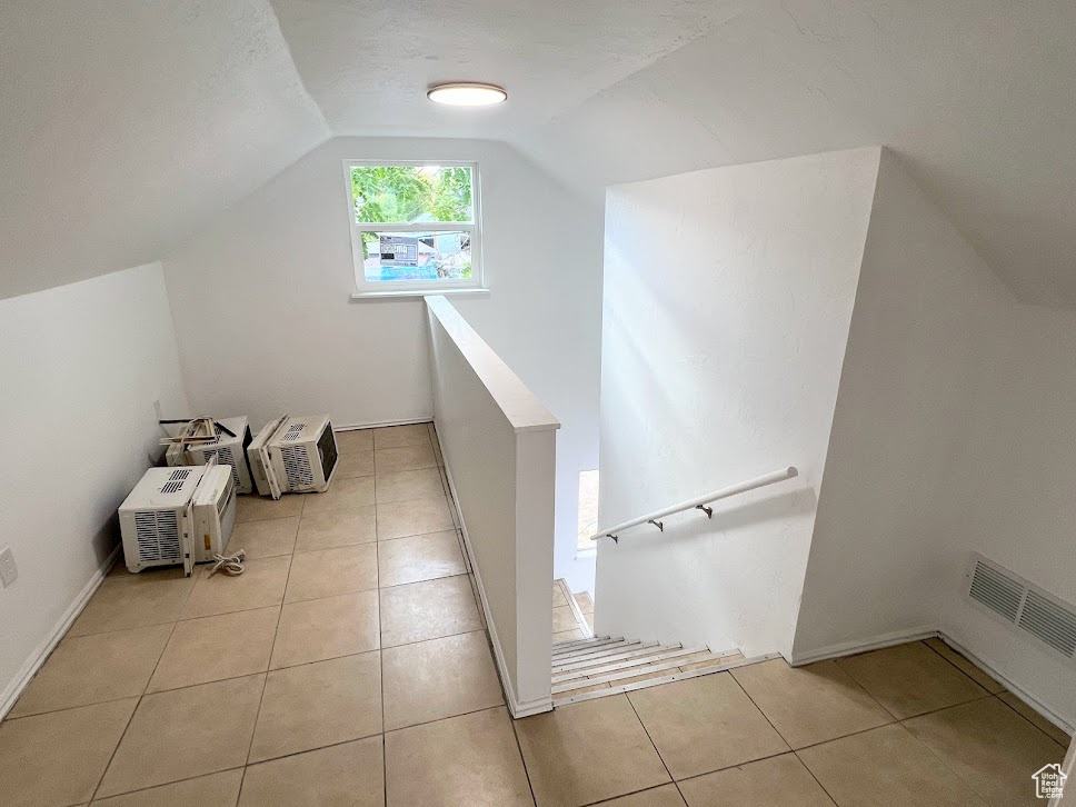 Additional living space with light tile patterned flooring, a wall mounted air conditioner, and vaulted ceiling