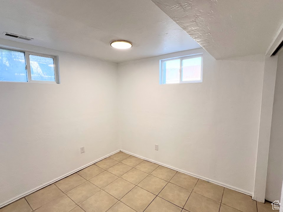 Basement with a textured ceiling, light tile patterned floors, and a wealth of natural light