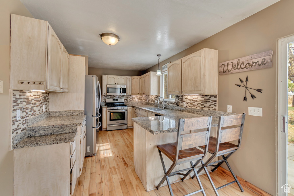 Kitchen with stainless steel appliances, light hardwood / wood-style floors, kitchen peninsula, hanging light fixtures, and light brown cabinetry