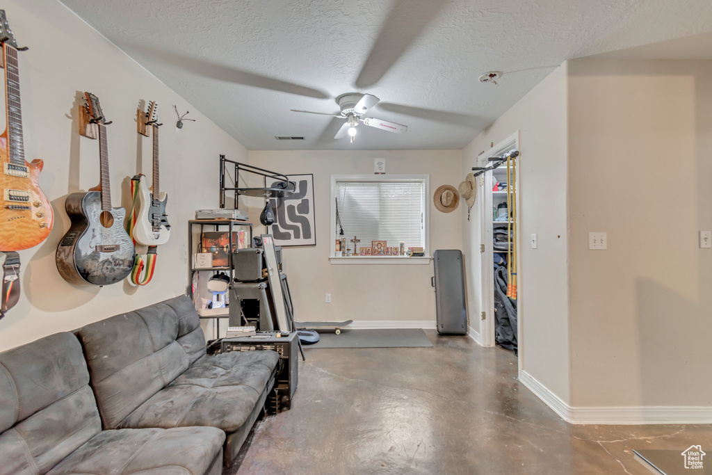 Exercise room with ceiling fan, concrete flooring, and a textured ceiling