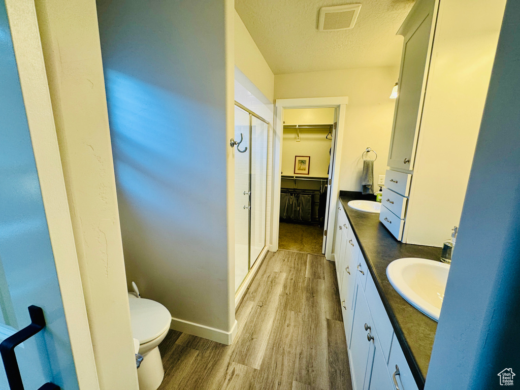 Bathroom with hardwood / wood-style floors, a shower with door, a textured ceiling, toilet, and vanity