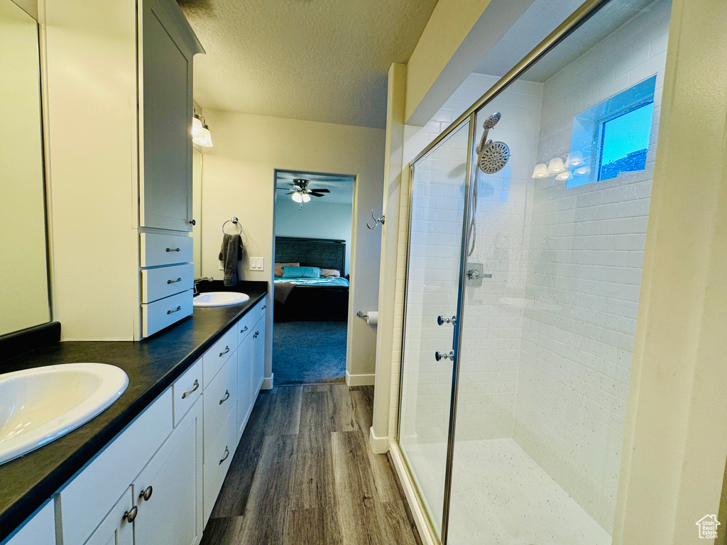 Bathroom featuring ceiling fan, a textured ceiling, hardwood / wood-style flooring, a shower with shower door, and vanity