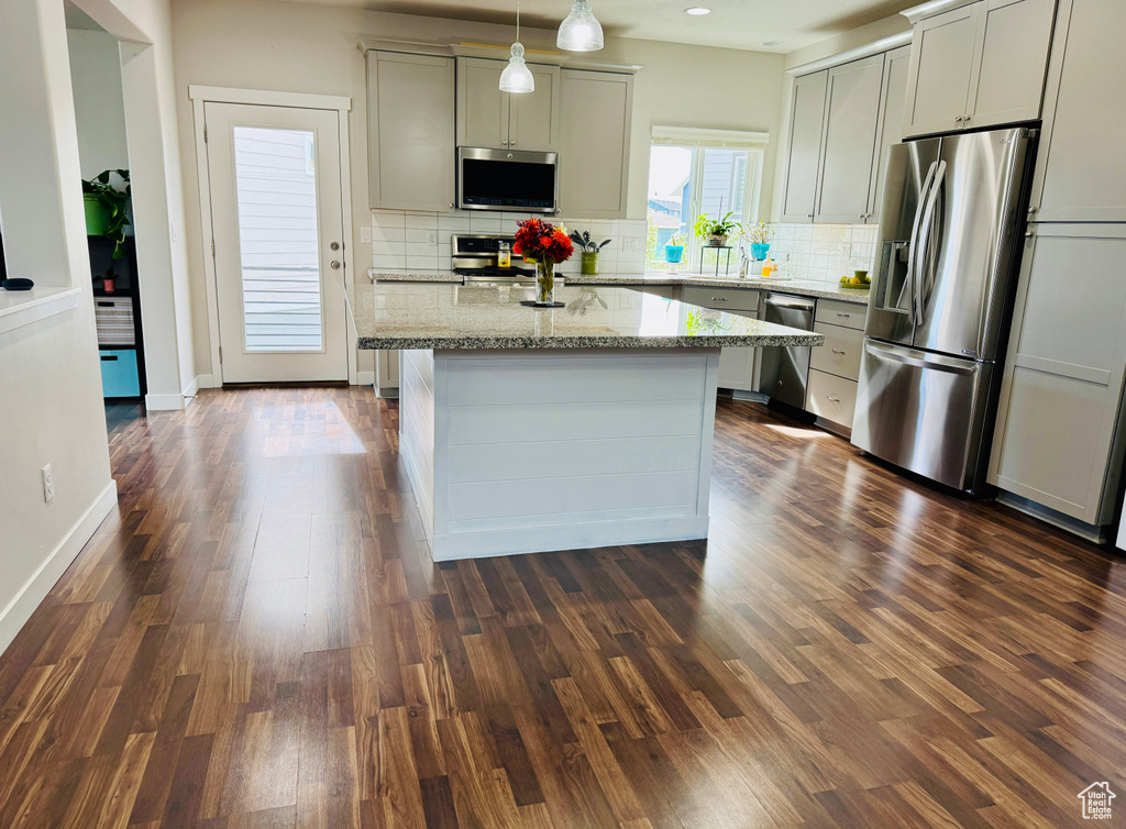 Kitchen featuring decorative backsplash, dark hardwood / wood-style flooring, decorative light fixtures, light stone counters, and stainless steel appliances