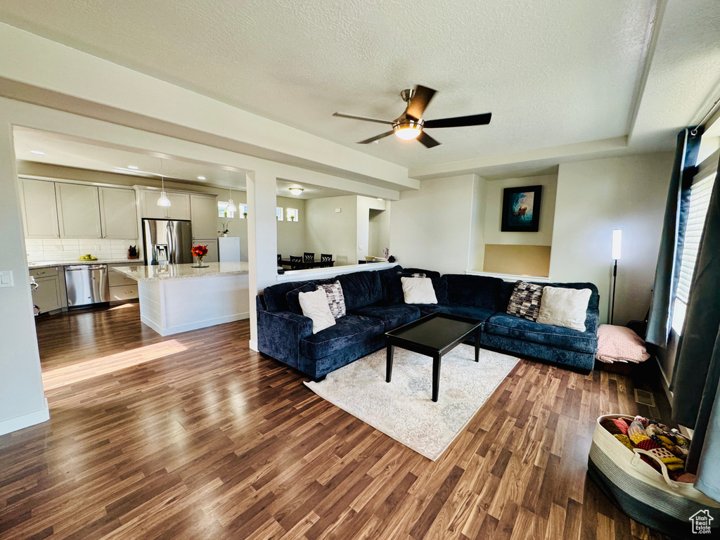 Living room featuring ceiling fan, dark wood-type flooring, and a textured ceiling