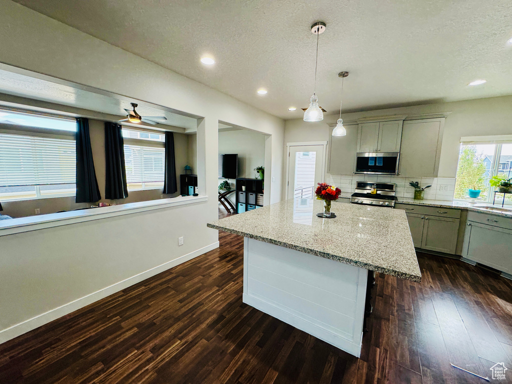 Kitchen featuring light stone countertops, stainless steel appliances, dark hardwood / wood-style flooring, and decorative light fixtures