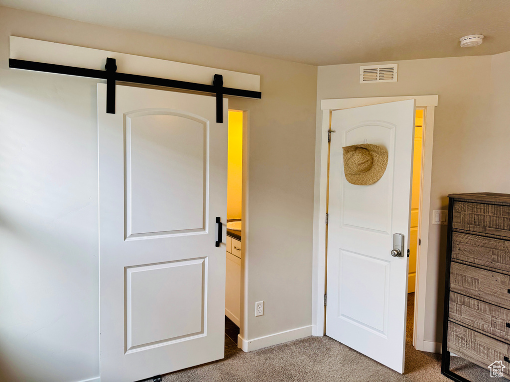 Unfurnished bedroom featuring ensuite bath, a barn door, and carpet flooring