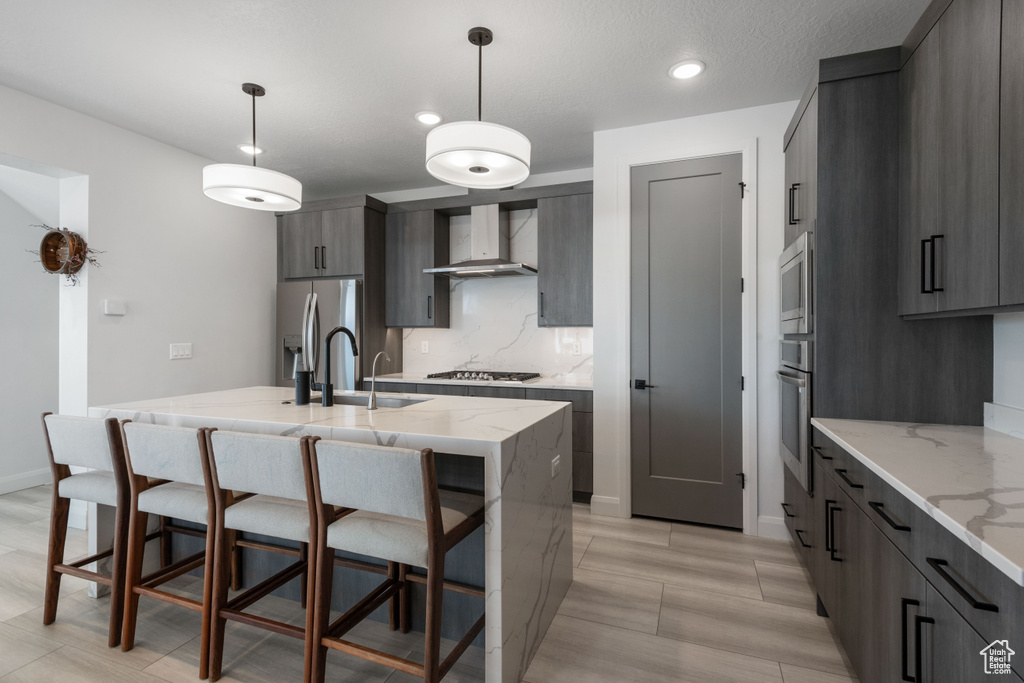 Kitchen with pendant lighting, gray cabinets, wall chimney range hood, and a kitchen breakfast bar