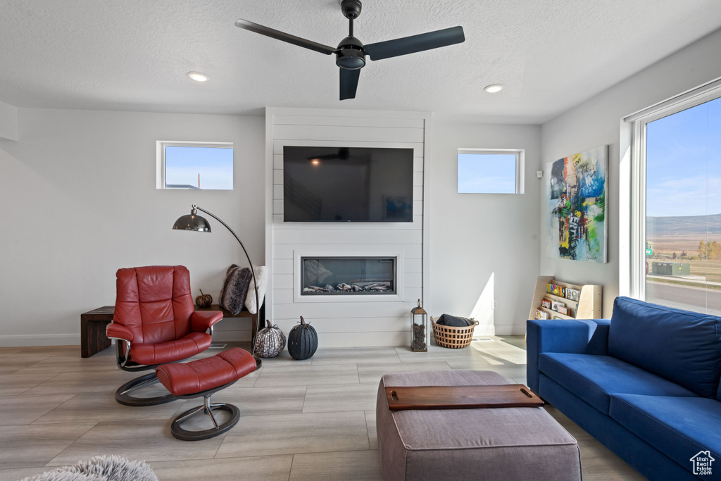 Living room featuring ceiling fan, a textured ceiling, a large fireplace, and a healthy amount of sunlight