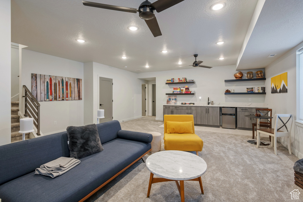 Carpeted living room with ceiling fan, sink, and a textured ceiling