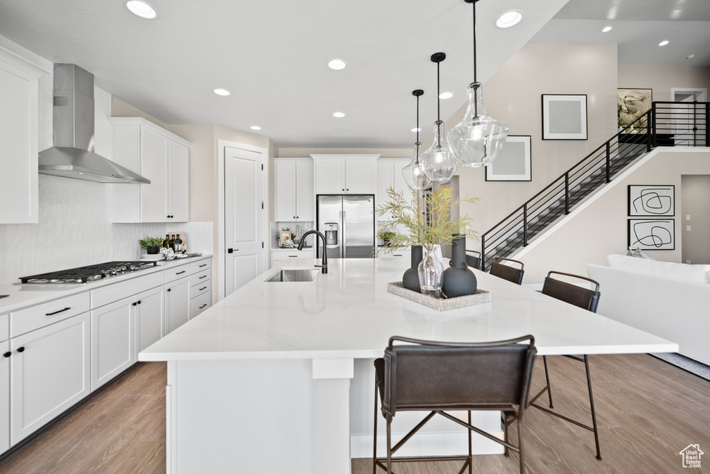 Kitchen featuring wall chimney range hood, appliances with stainless steel finishes, and a large island with sink