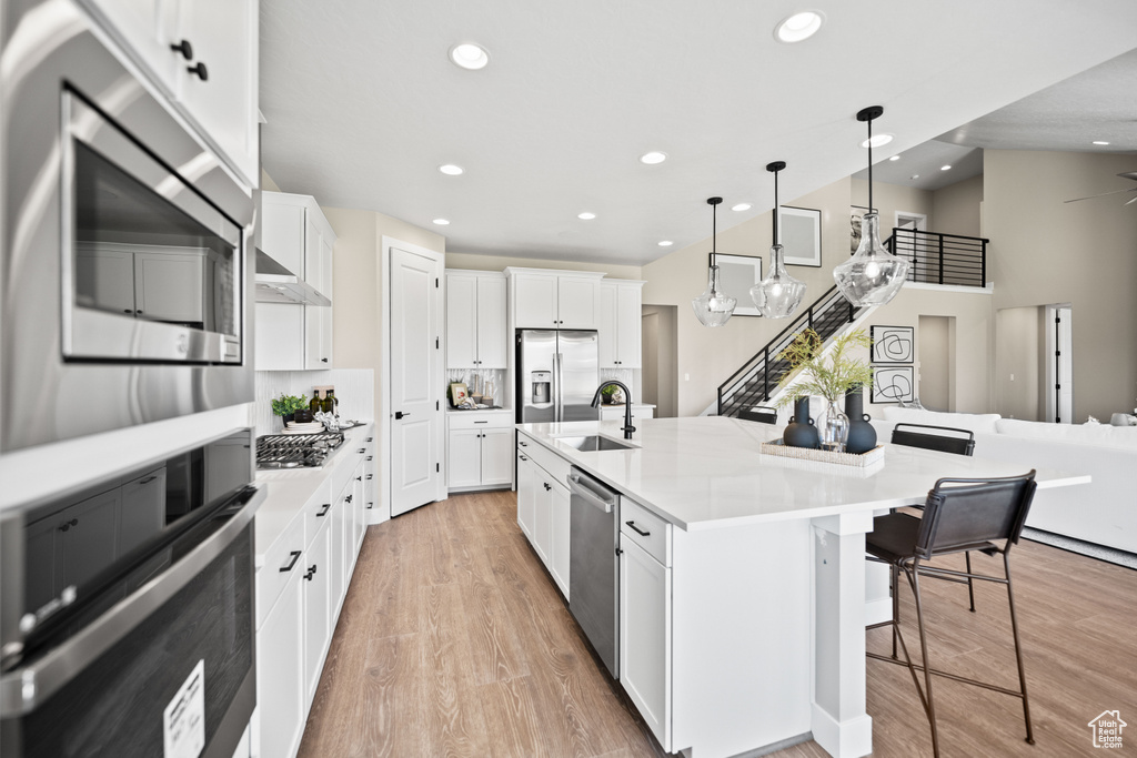 Kitchen featuring sink, pendant lighting, white cabinetry, appliances with stainless steel finishes, and a center island with sink