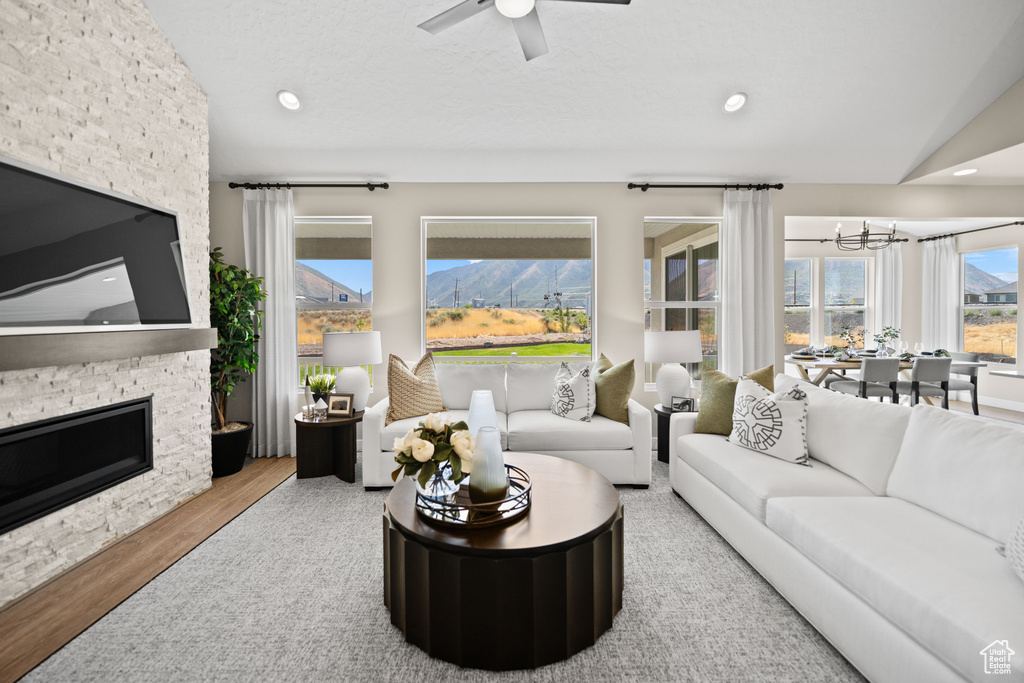 Living room with lofted ceiling, wood-type flooring, ceiling fan with notable chandelier, and a stone fireplace