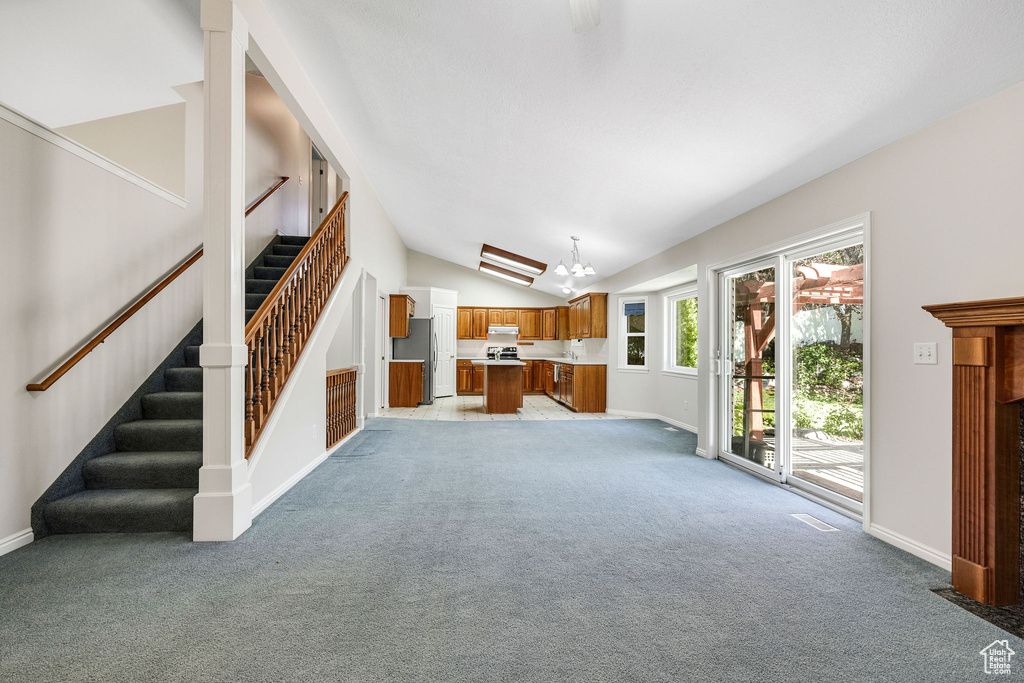 Unfurnished living room with light colored carpet, vaulted ceiling, and a chandelier