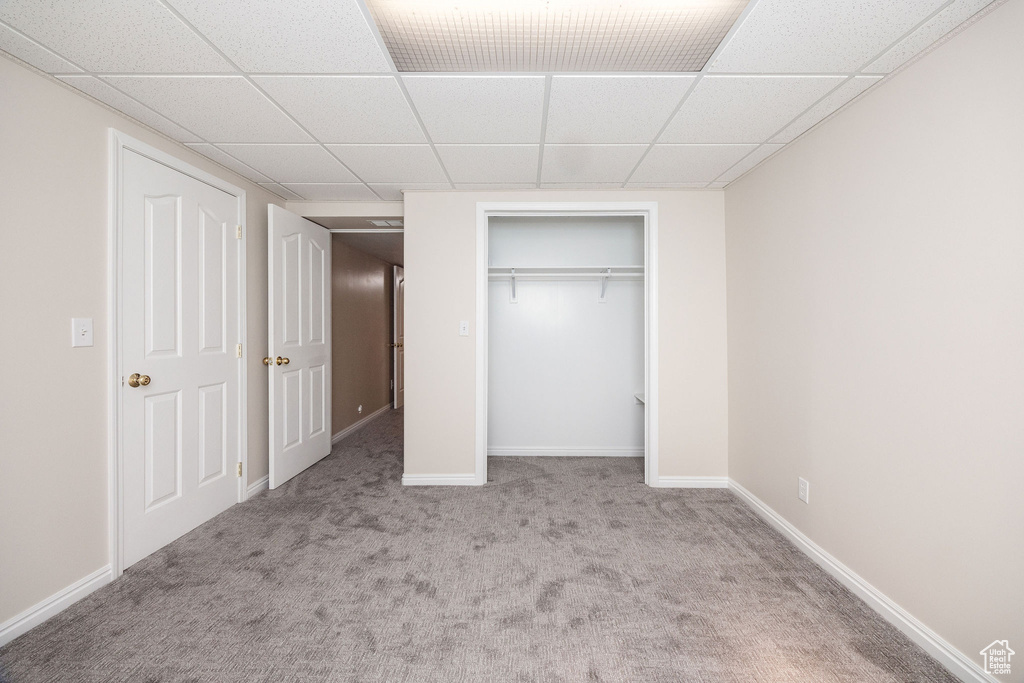 Unfurnished bedroom featuring a paneled ceiling, a closet, and light carpet