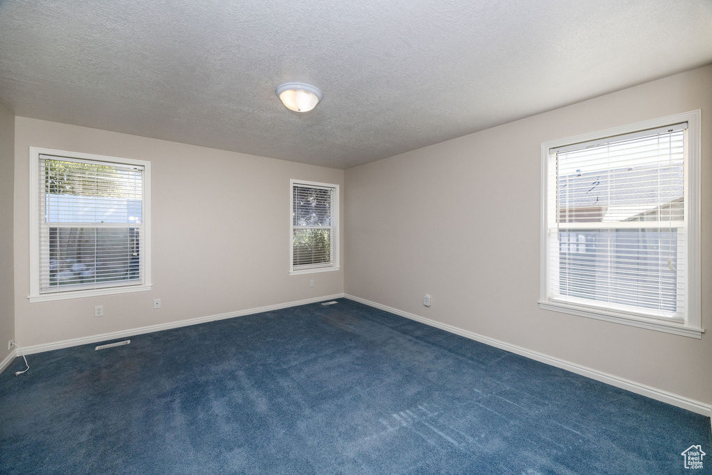 Unfurnished room featuring a textured ceiling and dark colored carpet