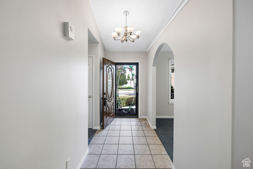 Tiled foyer entrance with ornamental molding, lofted ceiling, and a chandelier