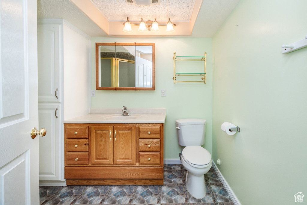 Bathroom featuring vanity, a shower with door, a tray ceiling, toilet, and a textured ceiling