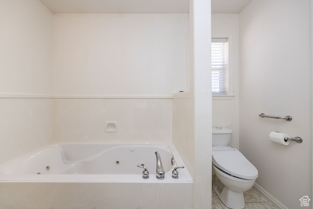 Bathroom with tile patterned flooring, a relaxing tiled tub, and toilet