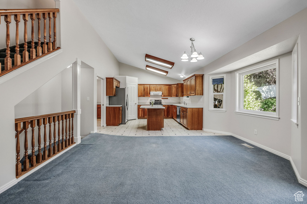 Kitchen with stainless steel fridge, a chandelier, a kitchen island, vaulted ceiling, and hanging light fixtures