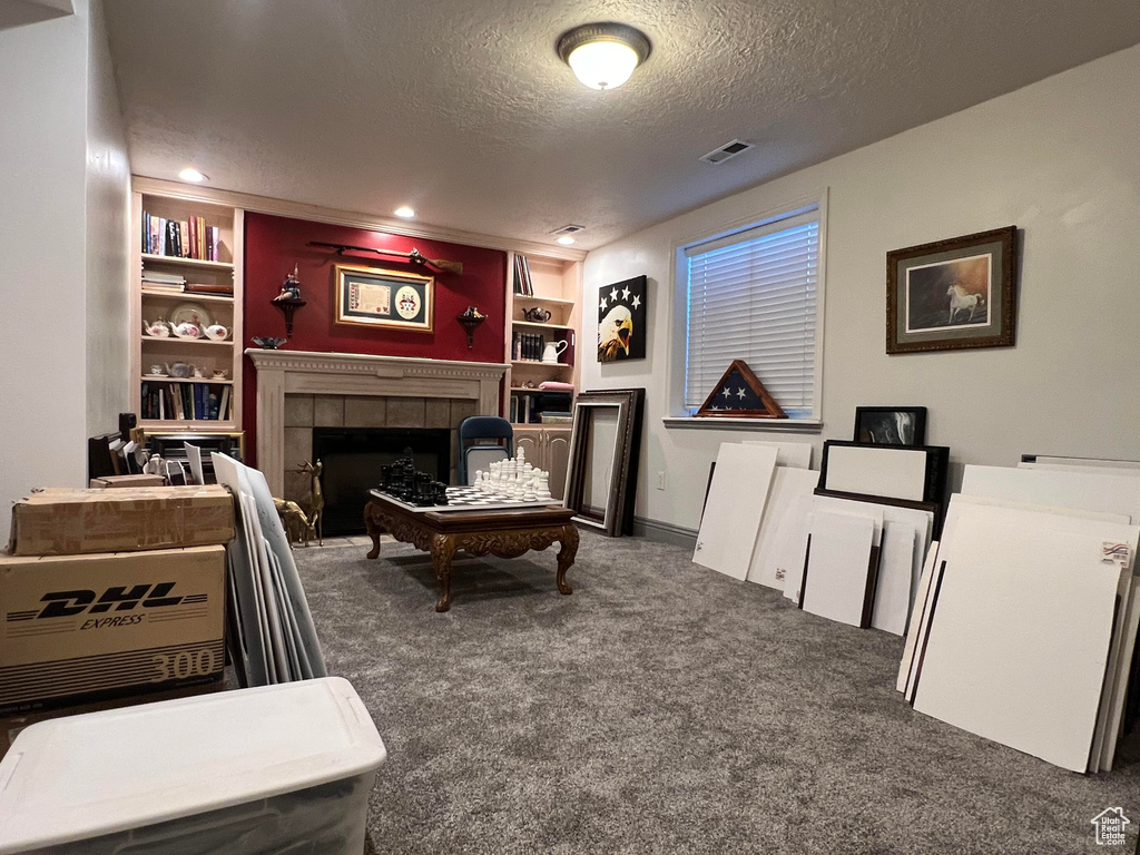 Interior space featuring a tile fireplace, built in features, dark carpet, and a textured ceiling