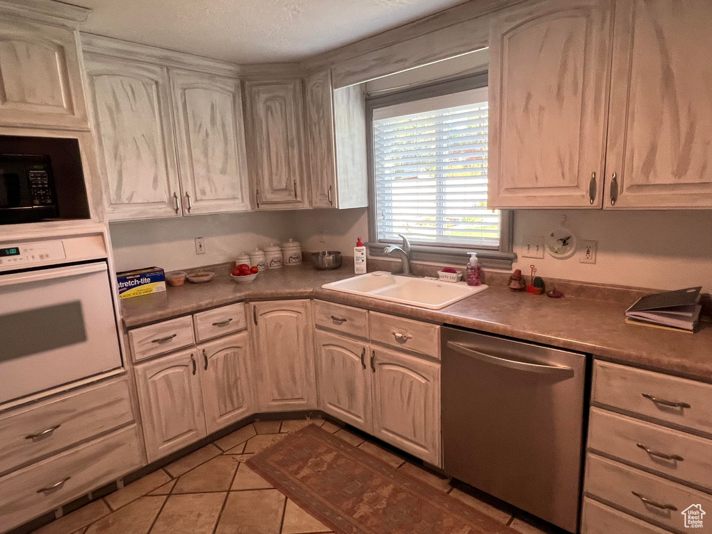 Kitchen featuring white oven, sink, stainless steel dishwasher, light tile patterned floors, and a textured ceiling