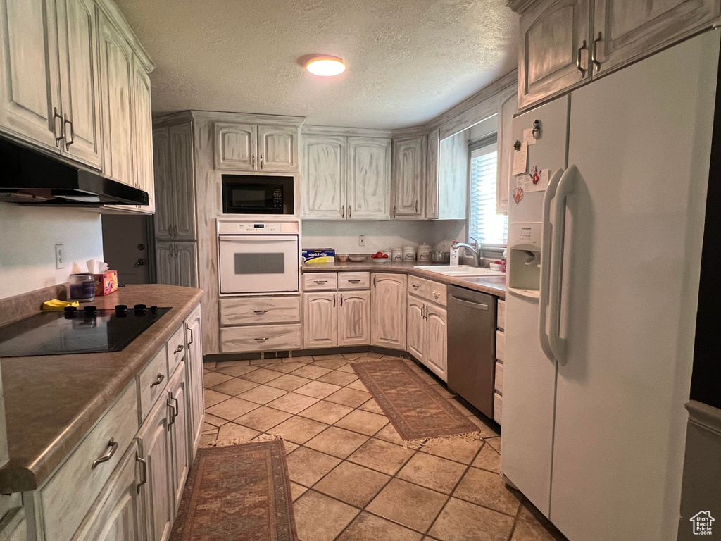 Kitchen with a textured ceiling, sink, light tile patterned floors, and black appliances