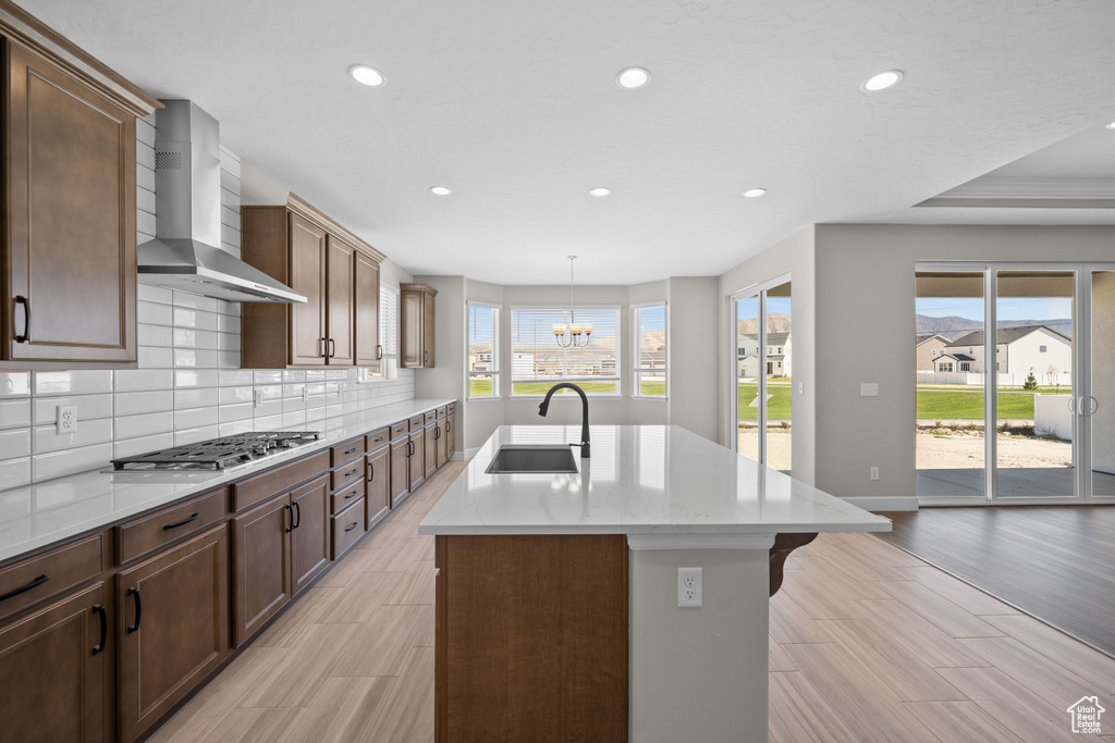 Kitchen with a center island with sink, wall chimney exhaust hood, stainless steel gas cooktop, and a wealth of natural light