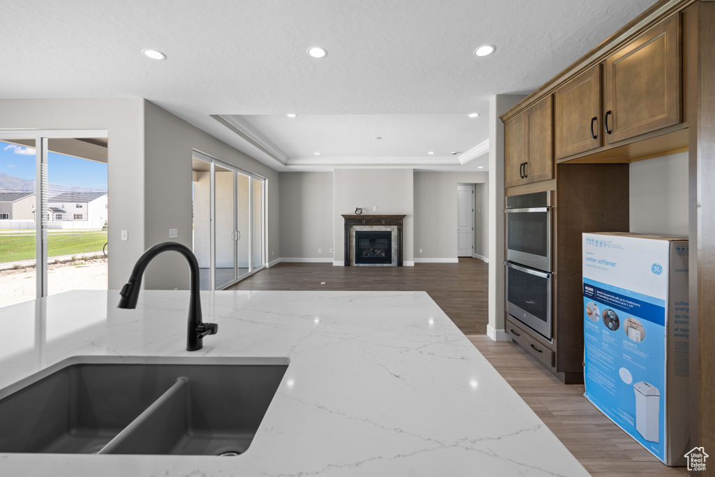 Kitchen featuring light stone countertops, a raised ceiling, double oven, sink, and dark hardwood / wood-style flooring