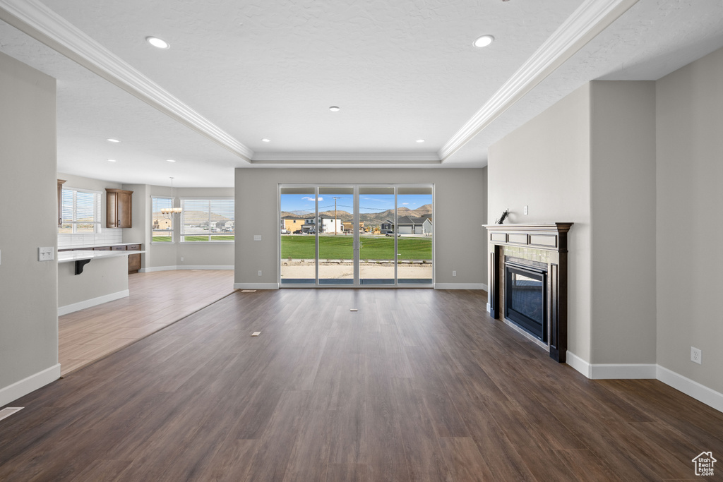 Unfurnished living room with ornamental molding, a tray ceiling, and dark hardwood / wood-style flooring