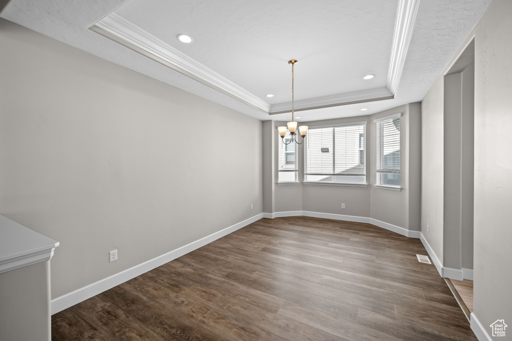 Unfurnished dining area featuring a raised ceiling, an inviting chandelier, ornamental molding, and hardwood / wood-style flooring