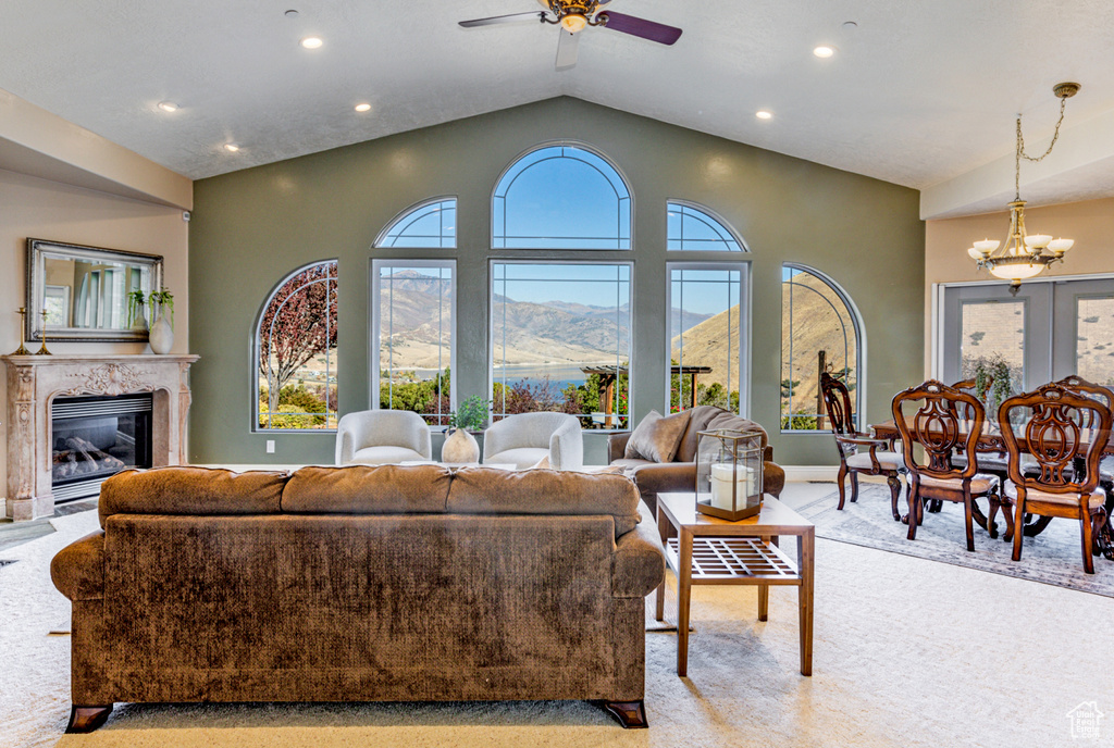 Living room featuring a mountain view, ceiling fan with notable chandelier, a premium fireplace, light carpet, and vaulted ceiling