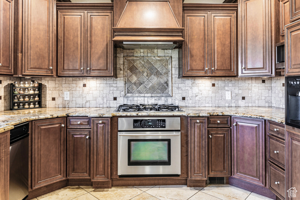 Kitchen with custom exhaust hood, light stone countertops, tasteful backsplash, and appliances with stainless steel finishes