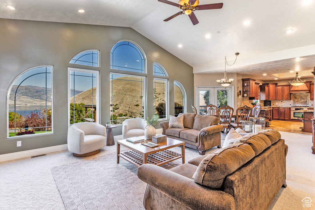 Living room featuring light colored carpet, ceiling fan with notable chandelier, and plenty of natural light