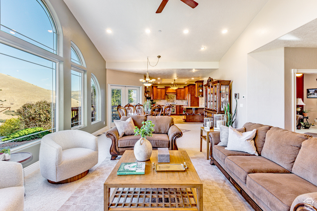 Carpeted living room with ceiling fan with notable chandelier and high vaulted ceiling