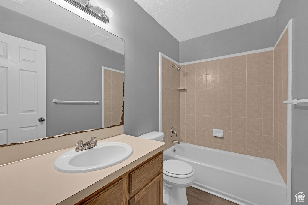 Full bathroom with hardwood / wood-style floors, vanity, tiled shower / bath combo, toilet, and a textured ceiling