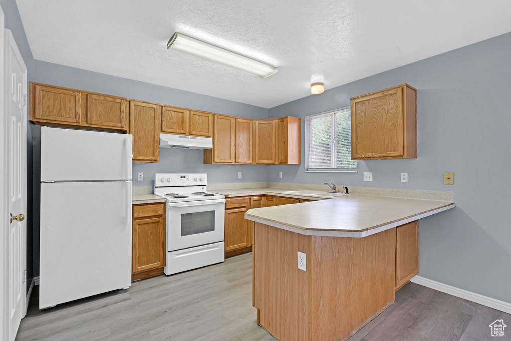 Kitchen with sink, kitchen peninsula, white appliances, a textured ceiling, and light hardwood / wood-style flooring