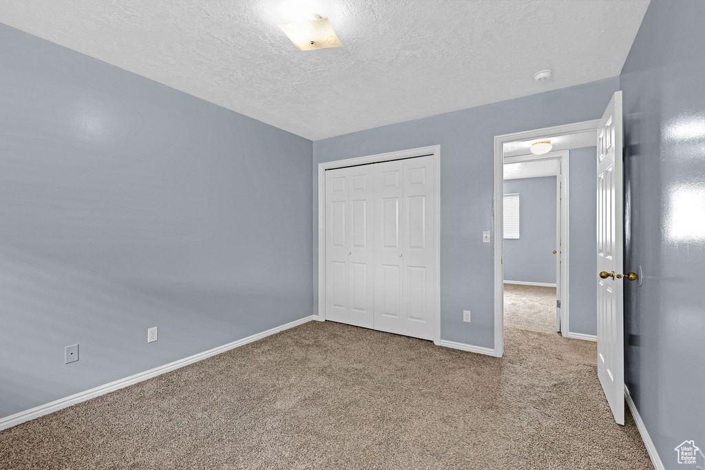 Unfurnished bedroom with light carpet, a closet, and a textured ceiling