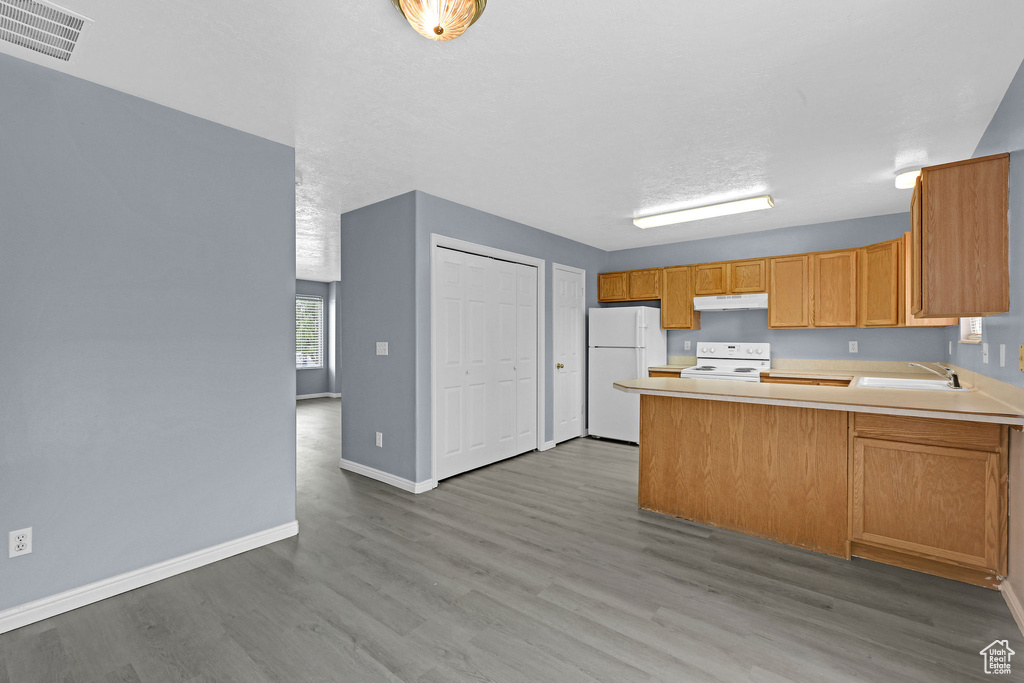 Kitchen featuring light wood-type flooring, white appliances, sink, kitchen peninsula, and a textured ceiling